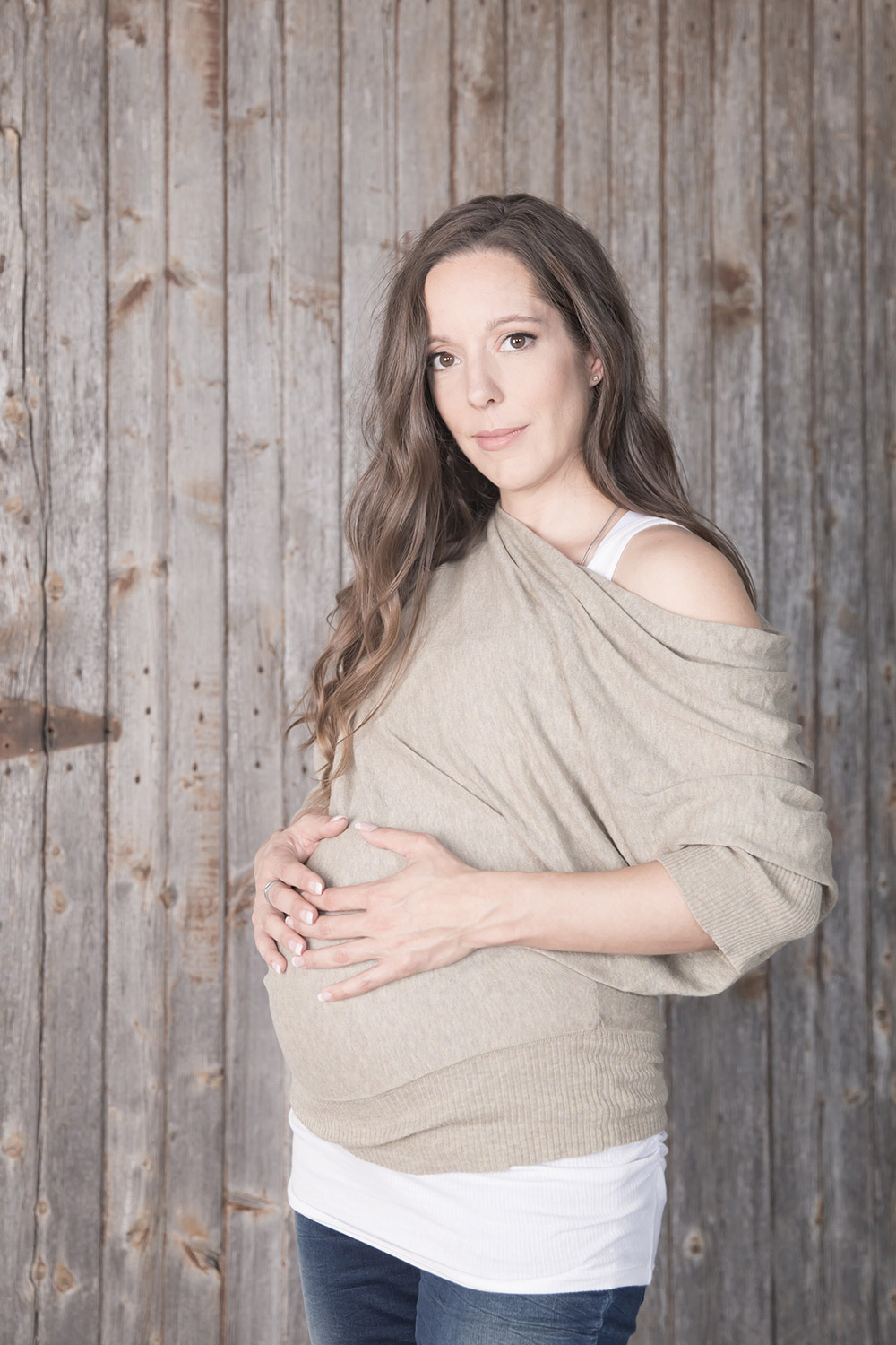a maternity photo a a woman holding her belly in front of a distressed wooden wall