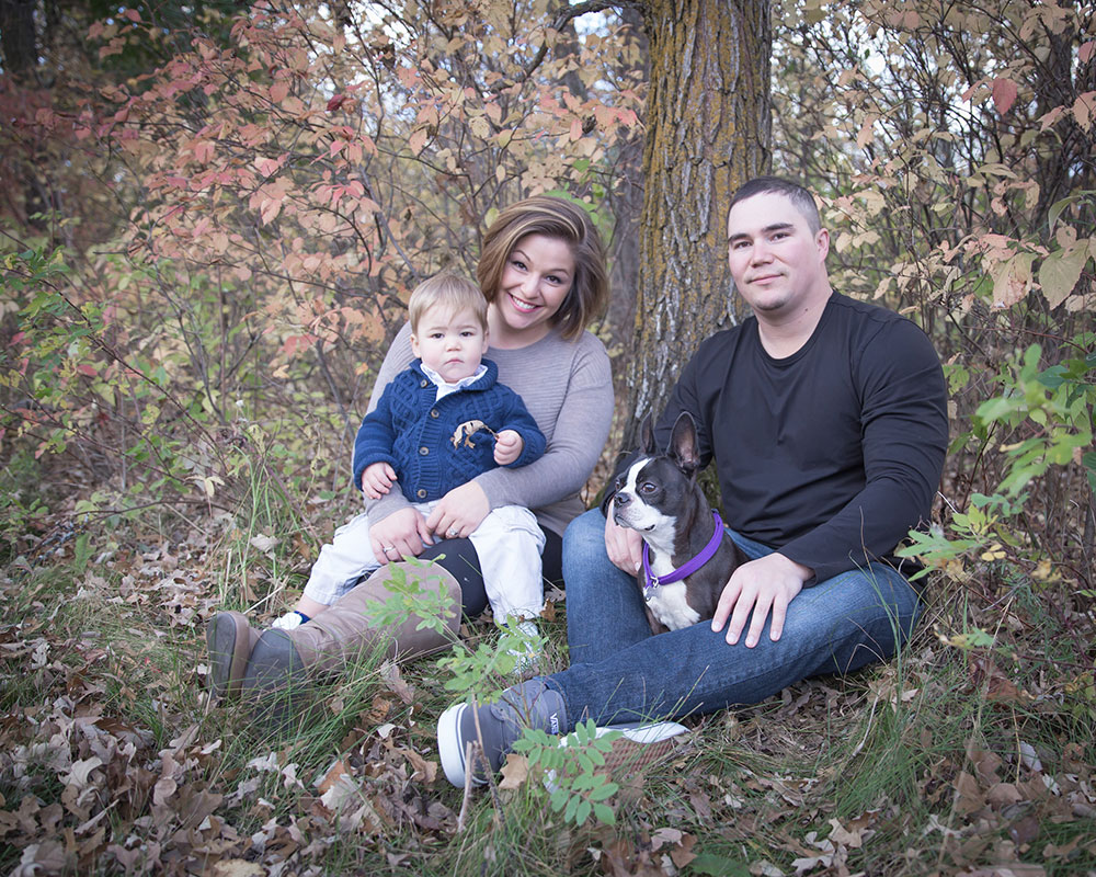 a photo of a young family with their son and dog in the fall leaves