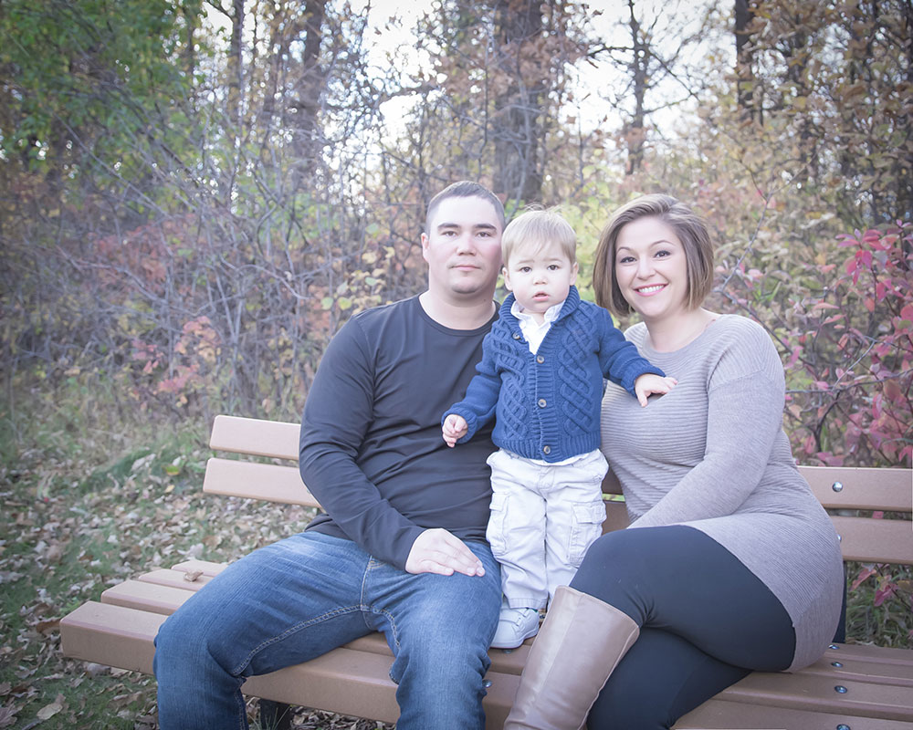 a photo of a young family sitting on a bench surrounded by fall leaves and colours