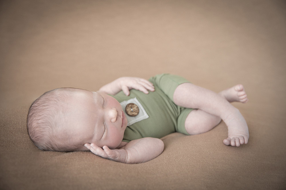 a sleeping newborn baby boy wearing a green romper