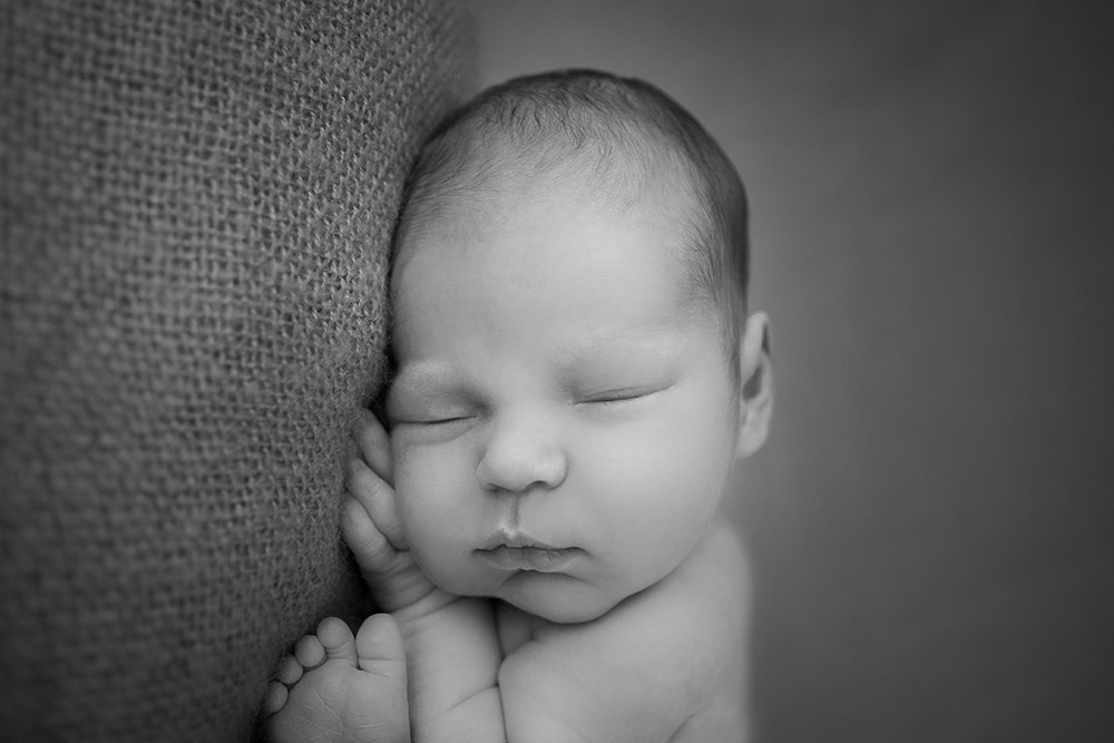a black and white photo of a posed, sleeping, newborn baby boy