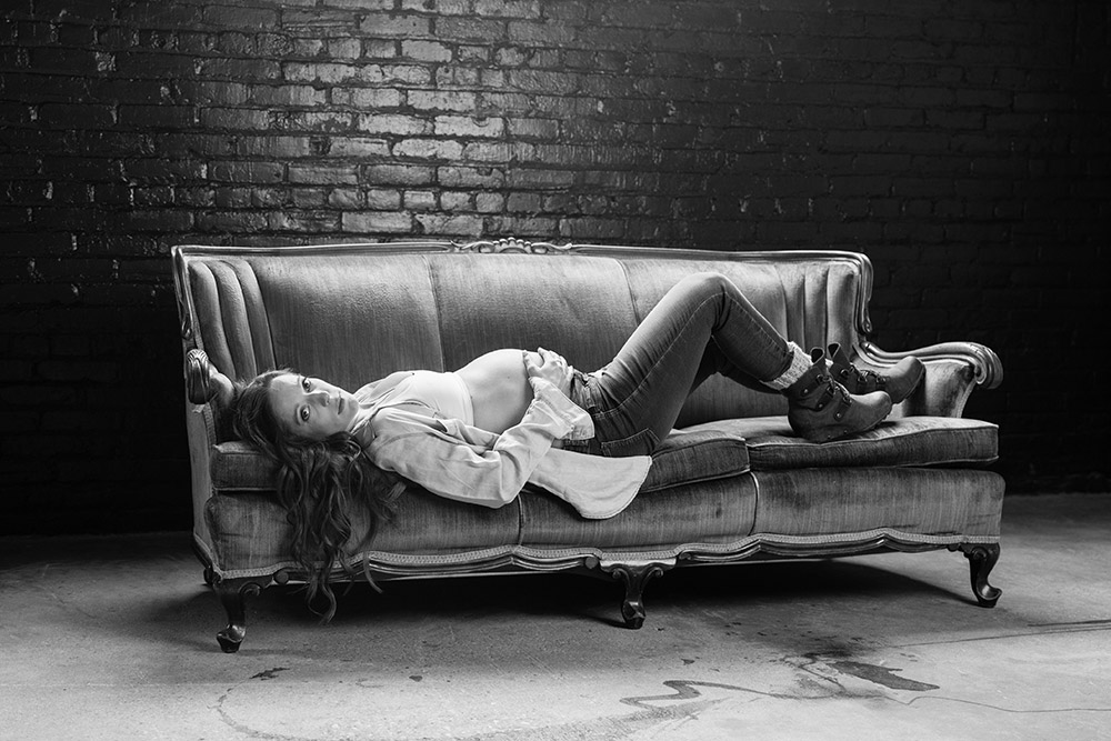 a maternity photo of a woman laying on a vintage couch