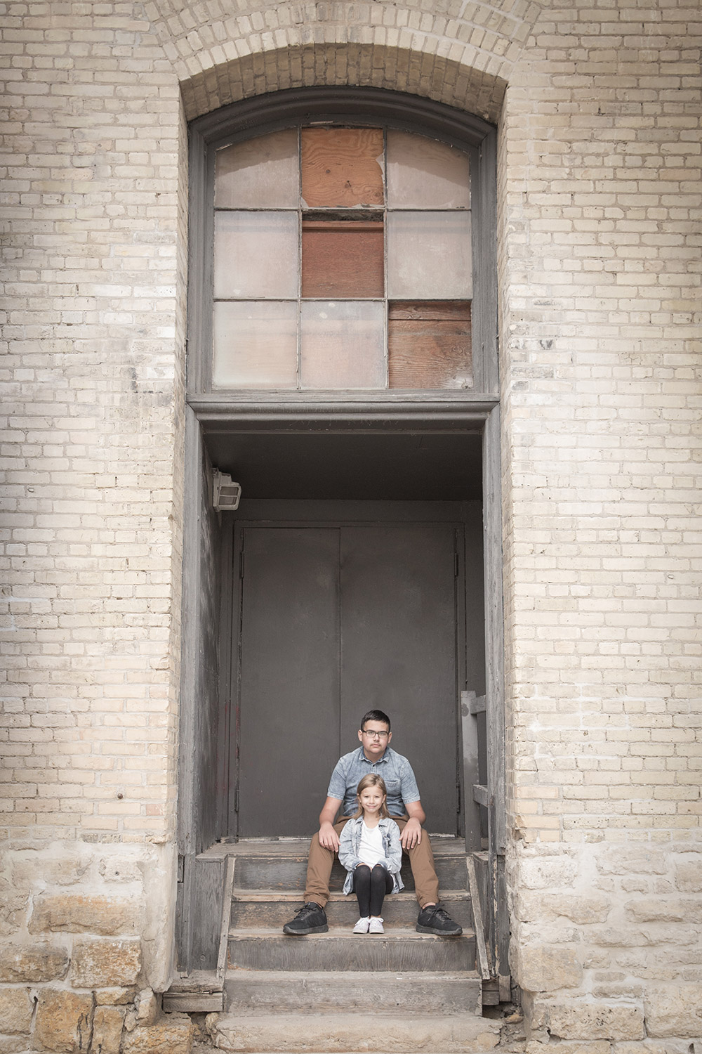 a photo of siblings sitting on concrete stairs in an old factory archway