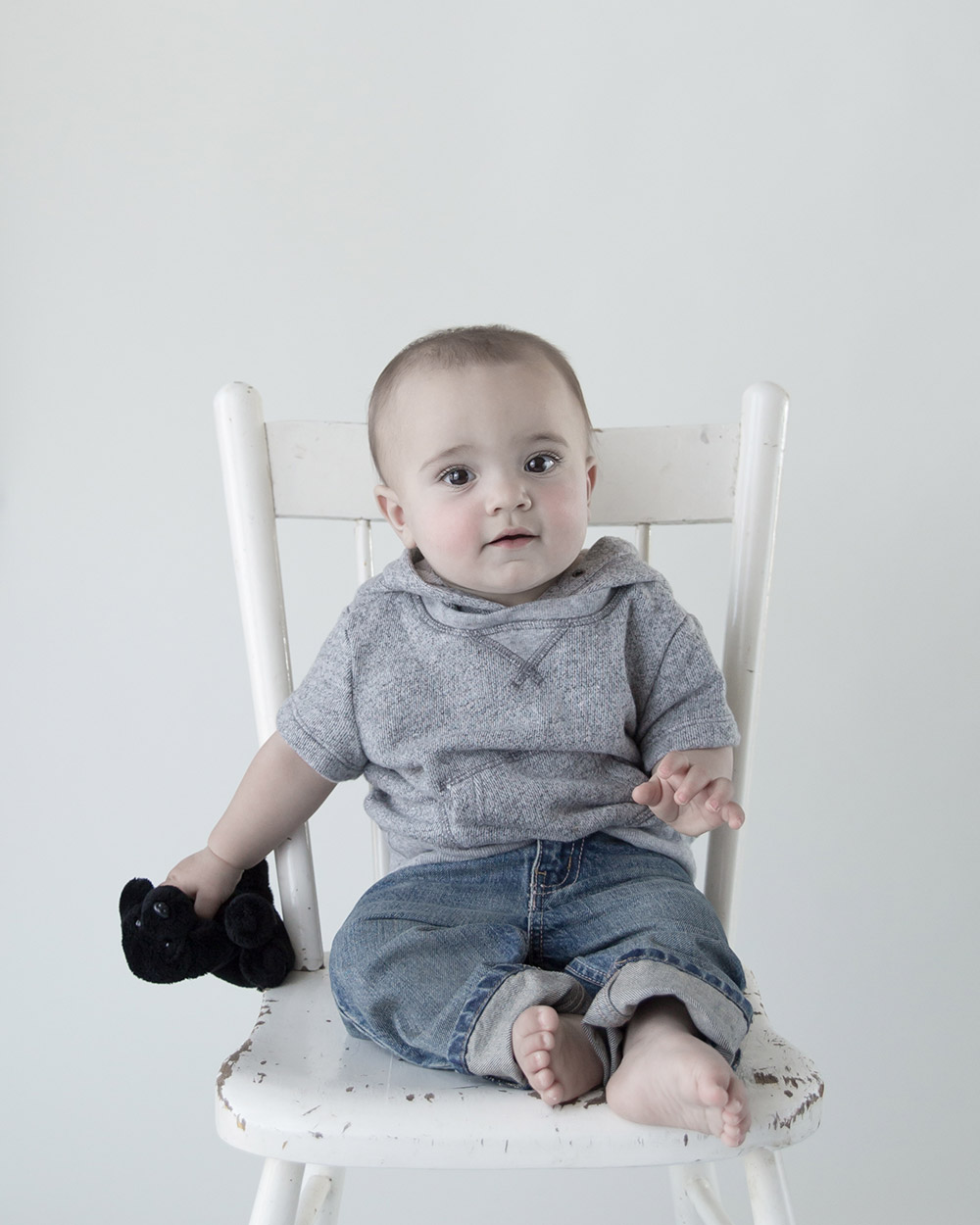 a photo of a baby boy sitting on a white chair holding a puppy toy