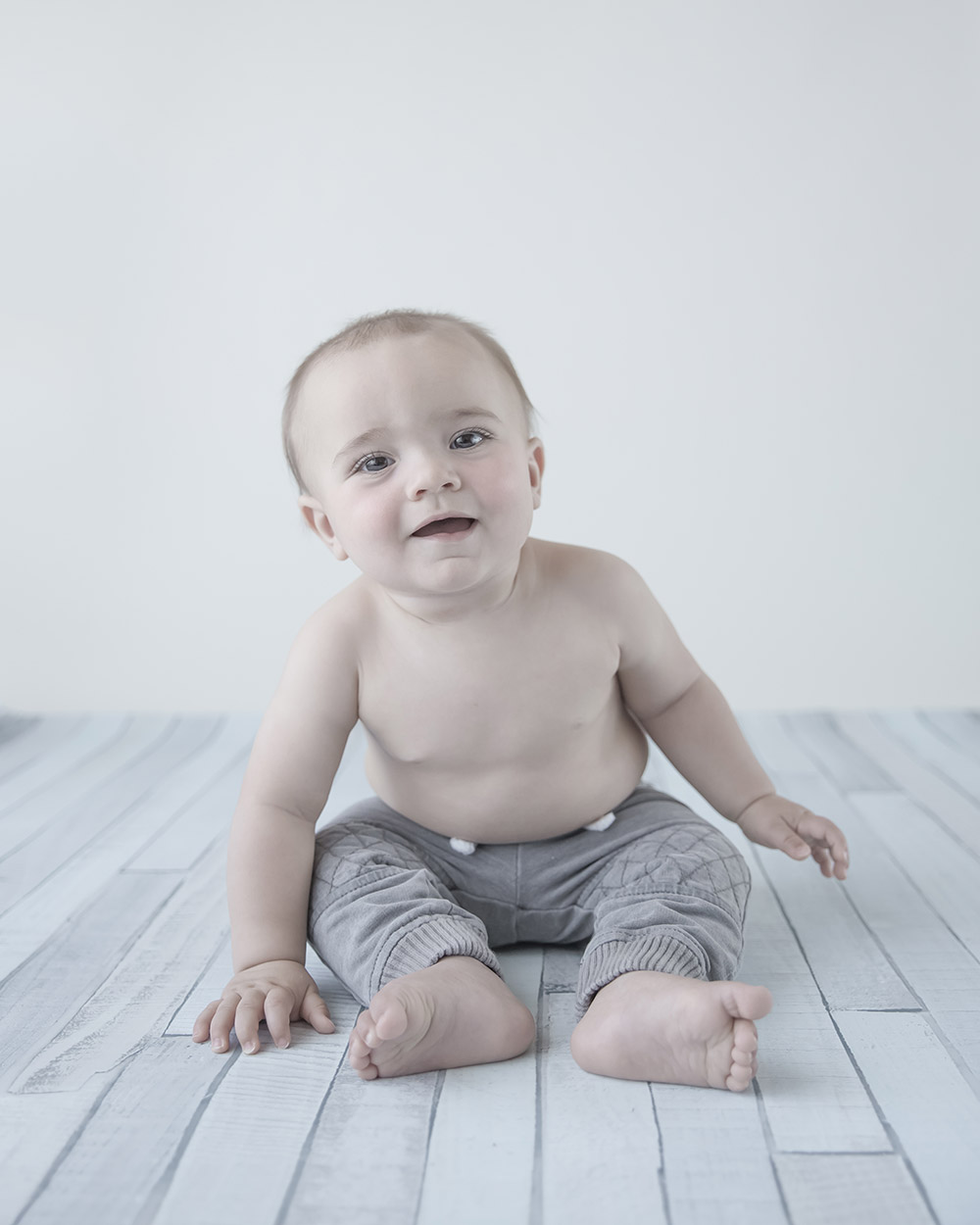 a photo of a baby boy smiling and sitting on a wood floordrop