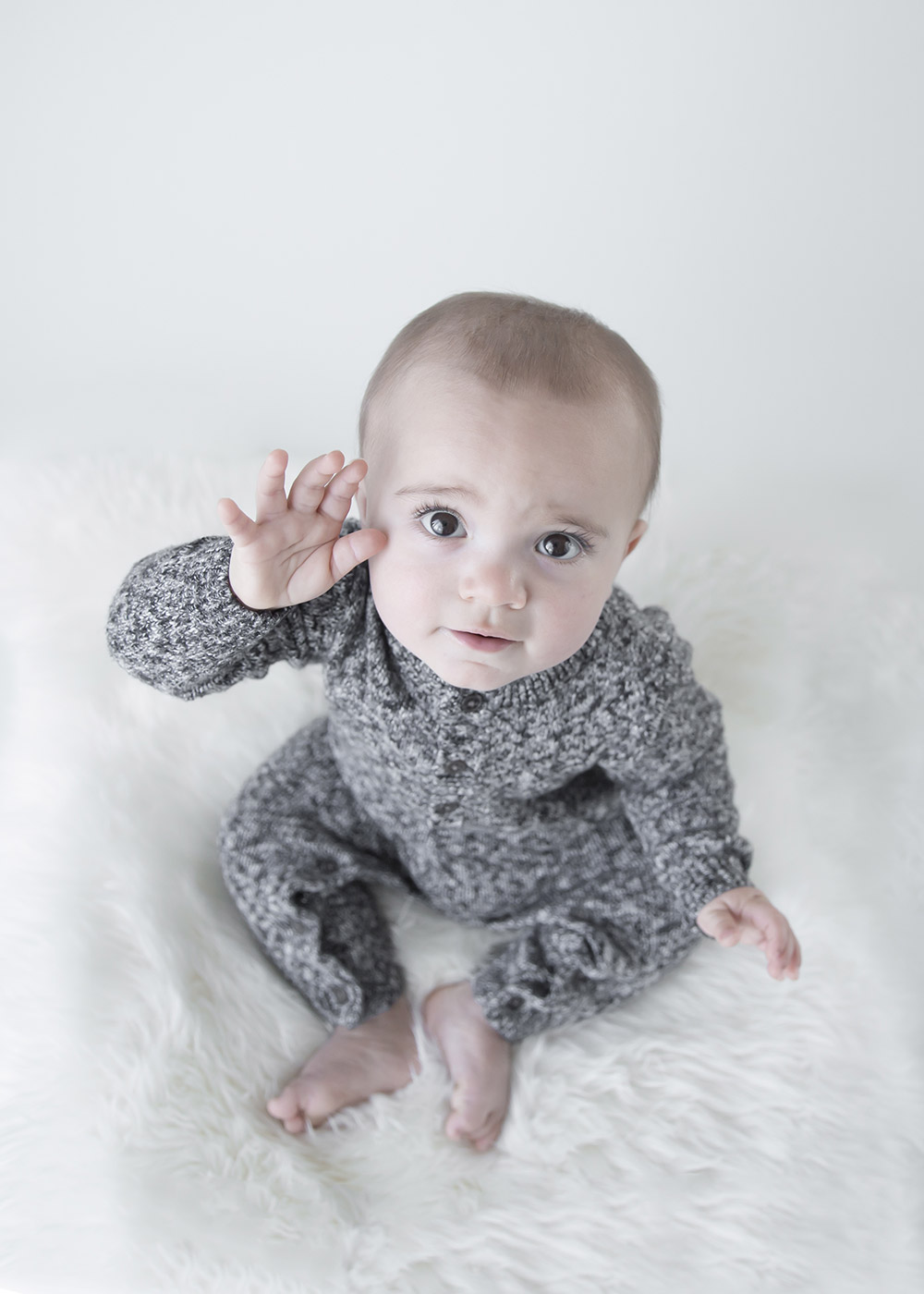 a photo of a baby boy sitting of a sheepskin rug and waving at the camera