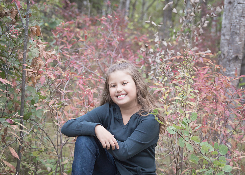 a photo of a young girl in the forest with colourful leaves