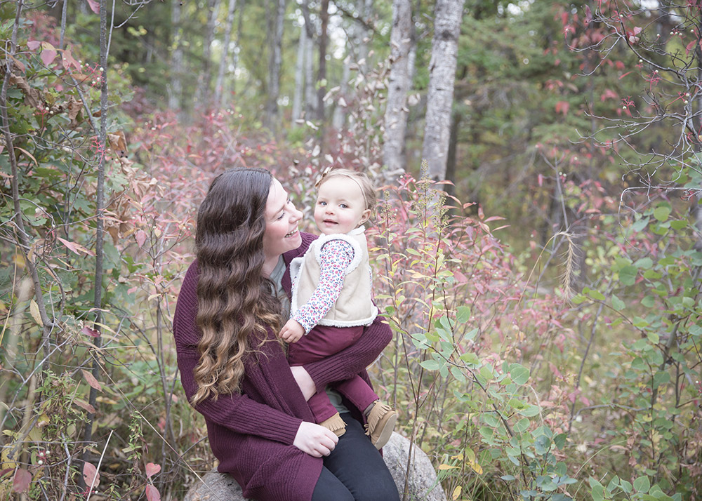 a photo of a mother smiling at her baby girl in the forest in fall