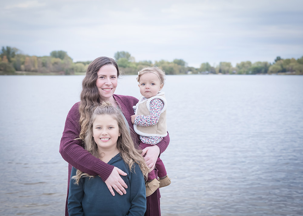 a photo of a mother and her daughters in front of a lake in fall