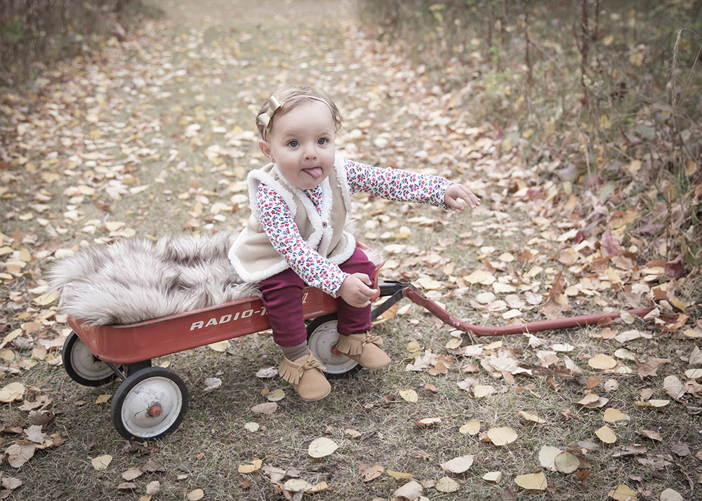 a photo of a baby girl sitting on a red wagon trying to stand up