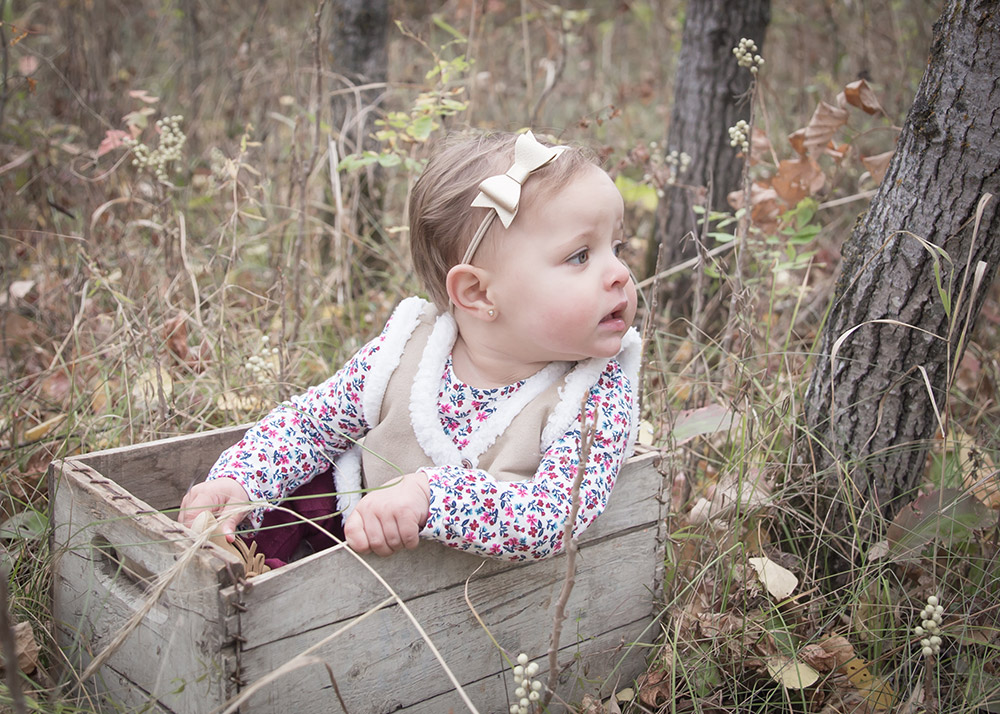 a photo of a baby girl sitting in a wooden crate in the forest