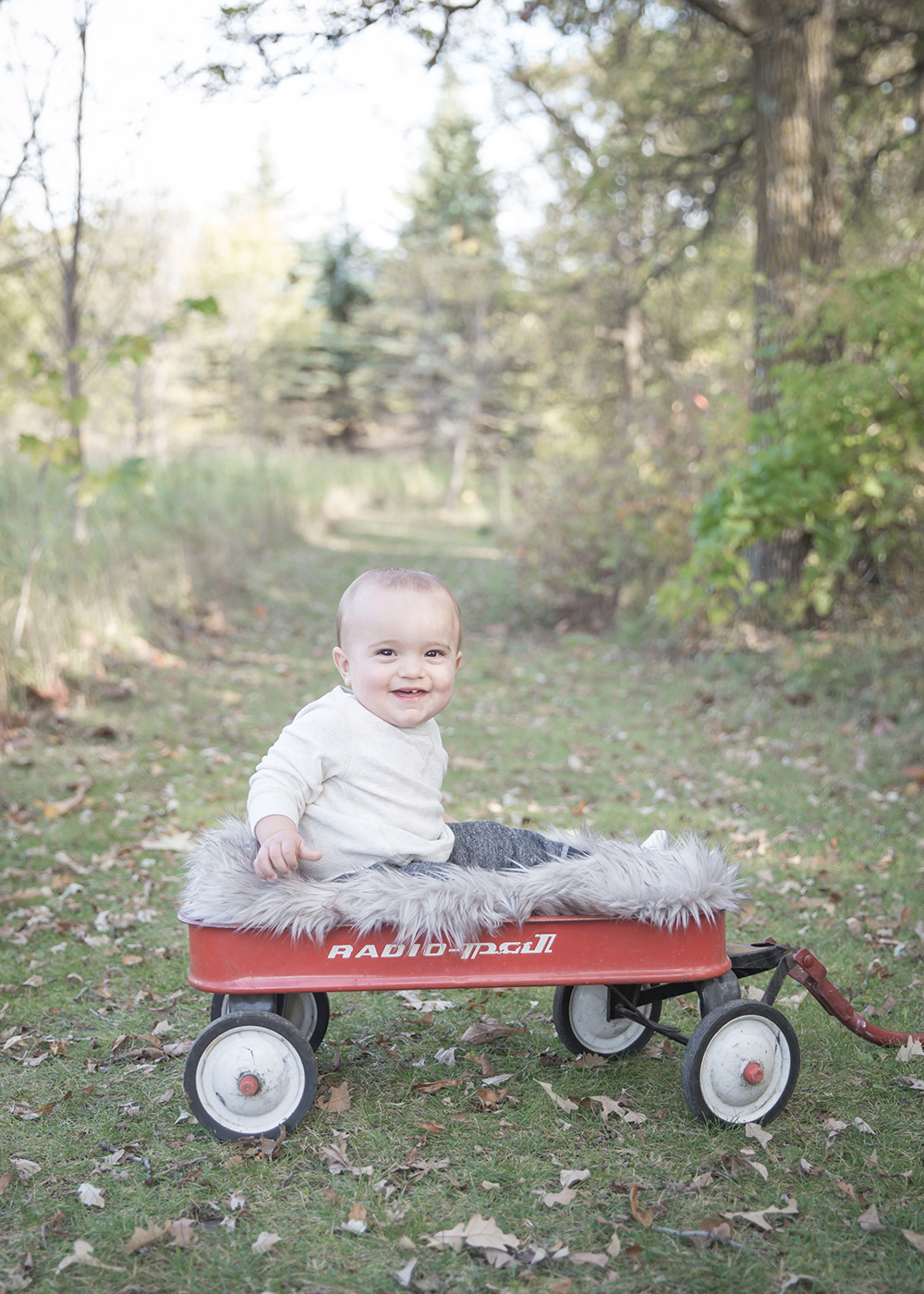 a photo of a baby boy sitting in a red wagon in fall