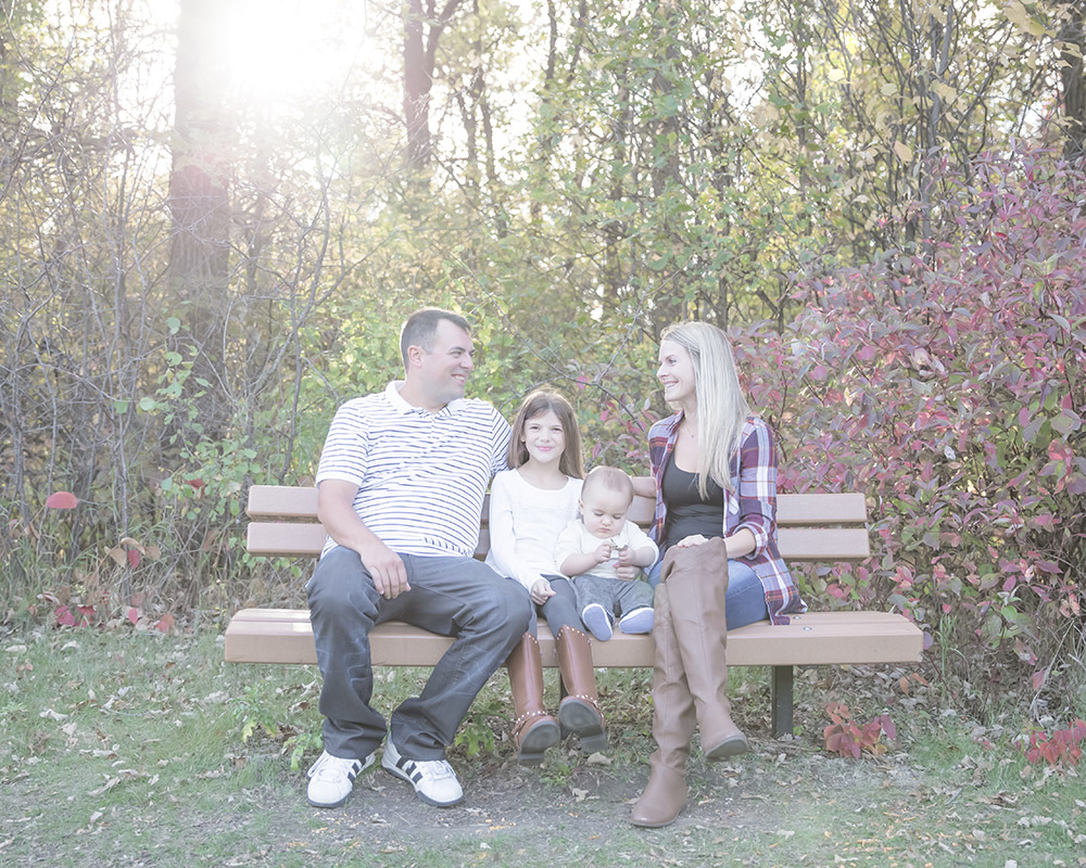 a photo of a young family sitting on a park bench in autumn