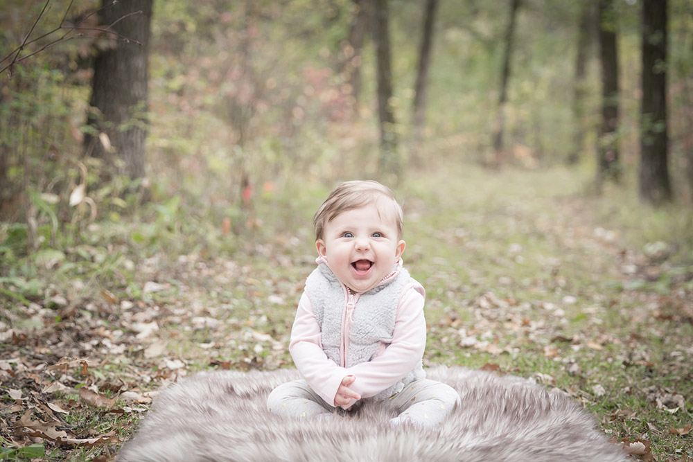 a photo of a baby girl sitting on a faux fur rug outside in the fall