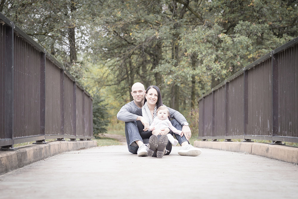 a photo of a young family sitting on a bridge in the fall