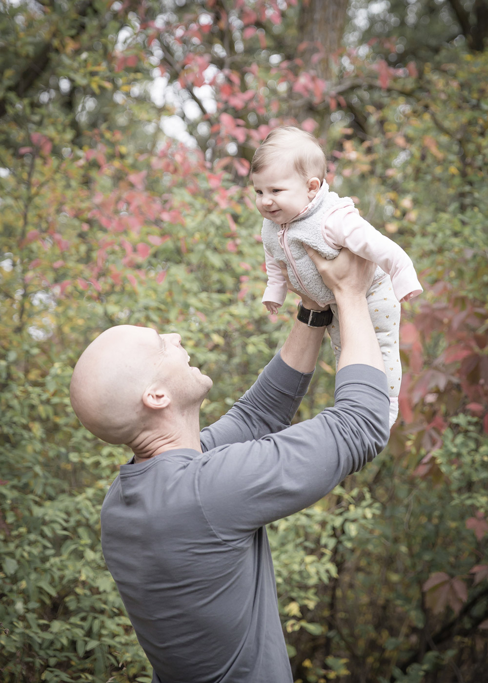 a photo of a father lifting his baby girl in the air in the fall time