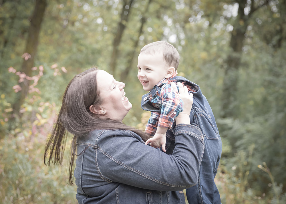 a photo of a mother lifting her little boy in the air in the fall time