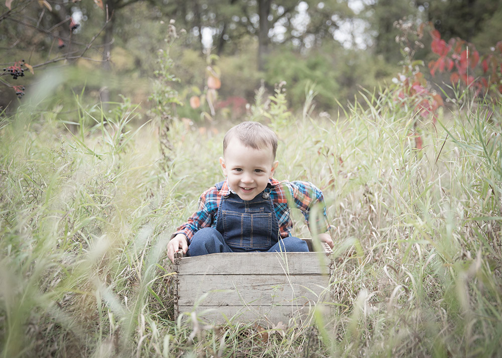 a little boy sitting in an old wooden crate in the fall time