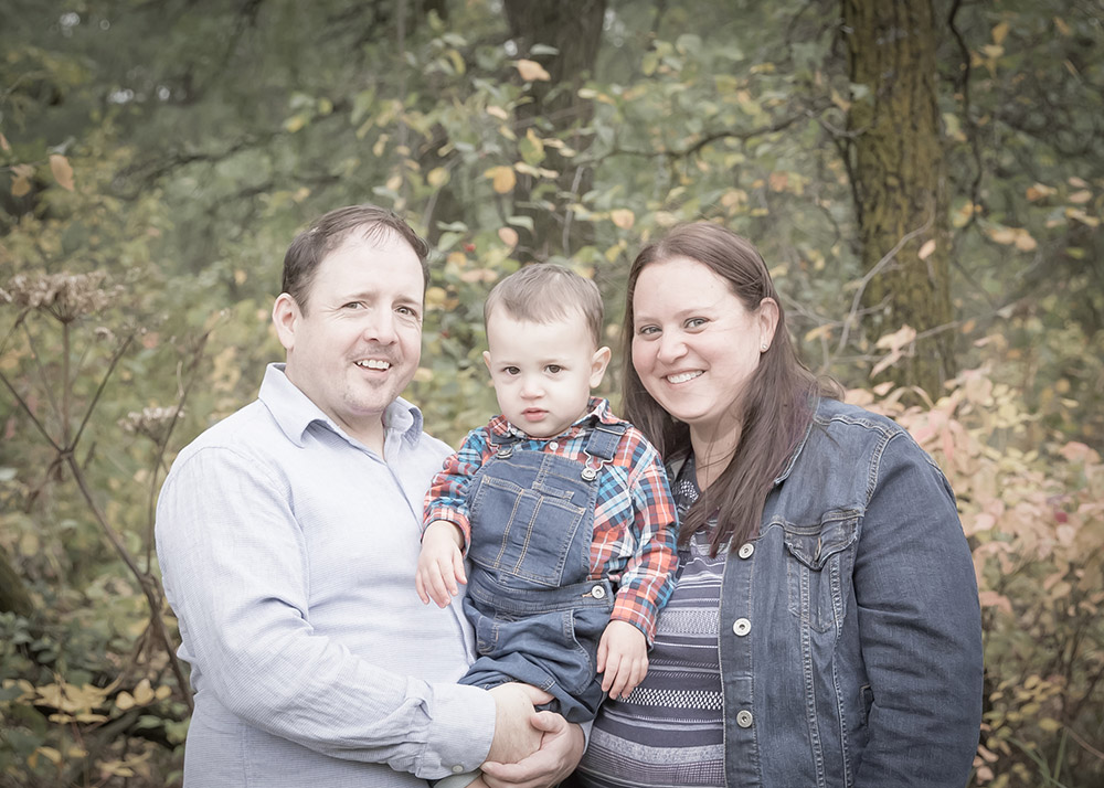 a family photo of a father, mother and son outside in the fall time