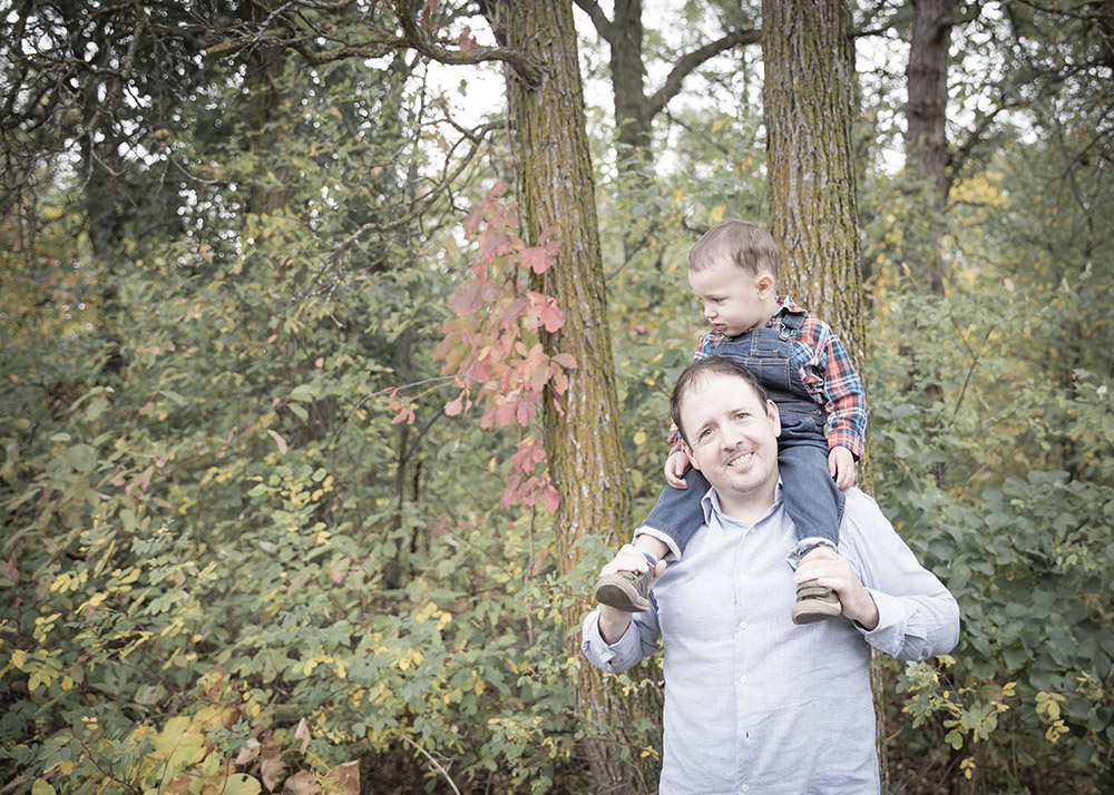 a little boy sitting on his fathers shoulders in the fall time
