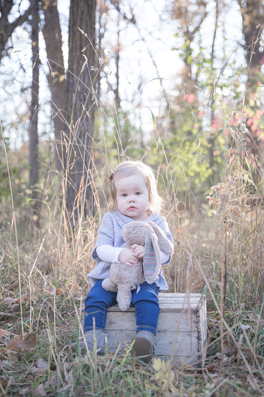 a photo of a little girl holding her bunny toy, sitting on an old wooden crate