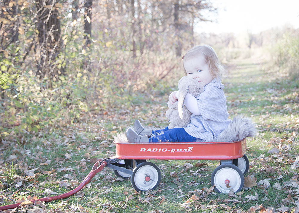a photo of a little girl snuggling her bunny toy while sitting in a red wagon