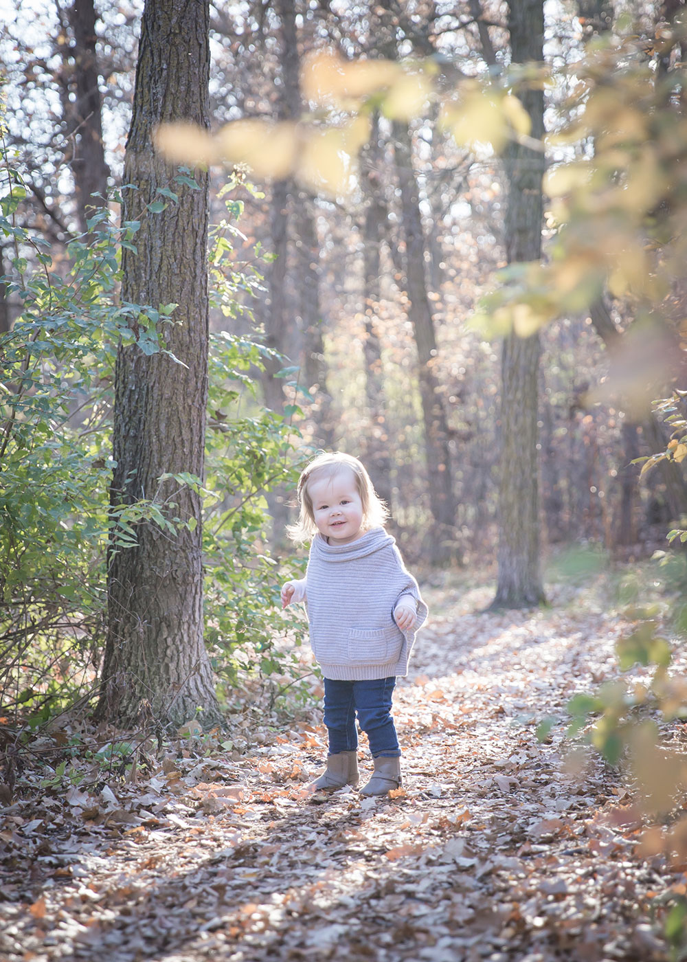 a photo of a little girl standing in the trees in the fall time