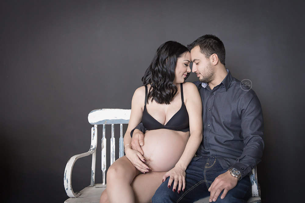 a photo of an expecting couple cuddling on a bench