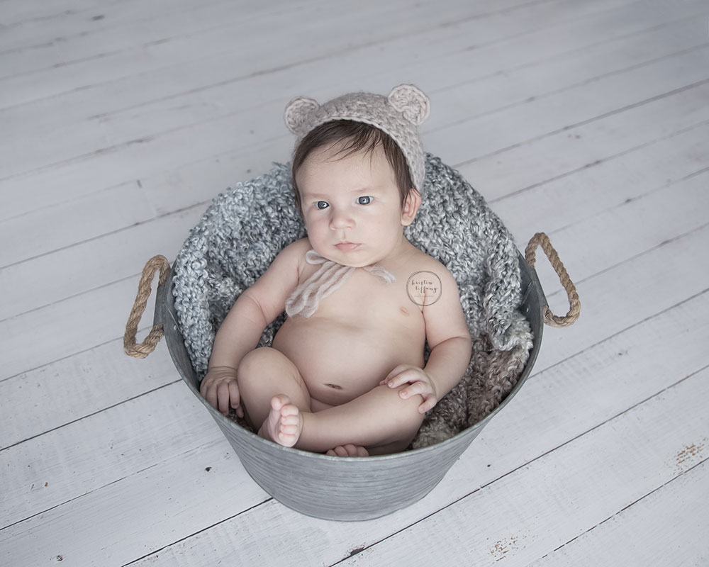 a photo of a baby boy sitting in a metal bucket with a bear bonnet
