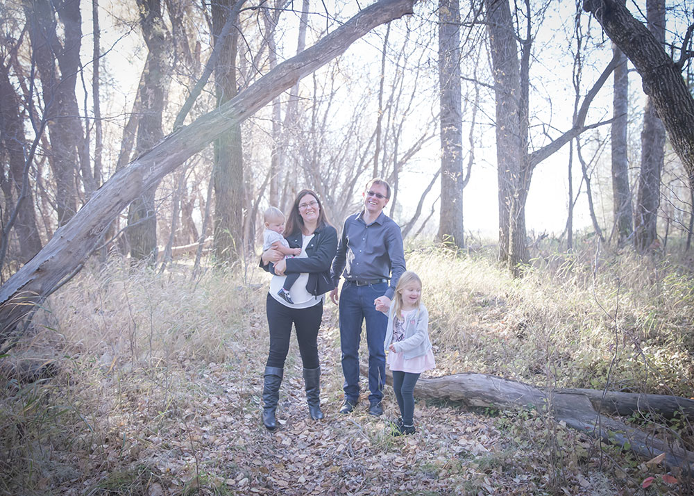 a photo of a young family in the woods in the fall time