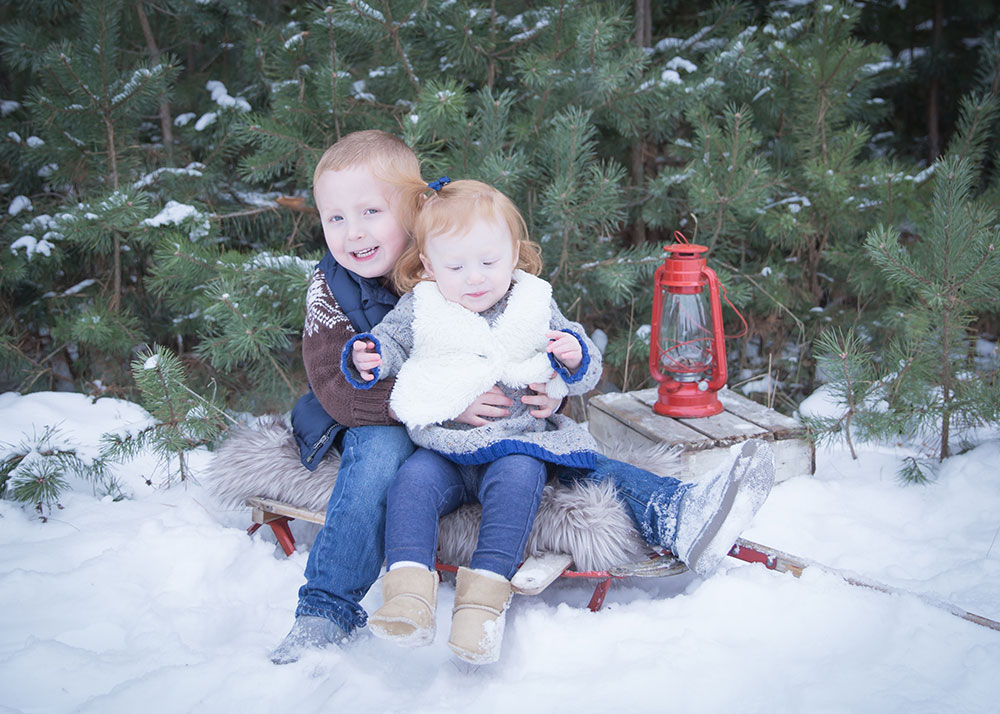 a photo of young siblings sitting on an old sled in the snow
