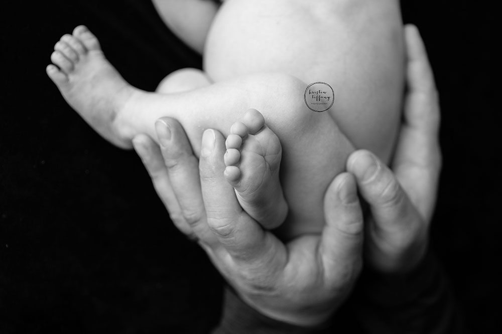 a black and white photo of a dad's hands holding his newborn son
