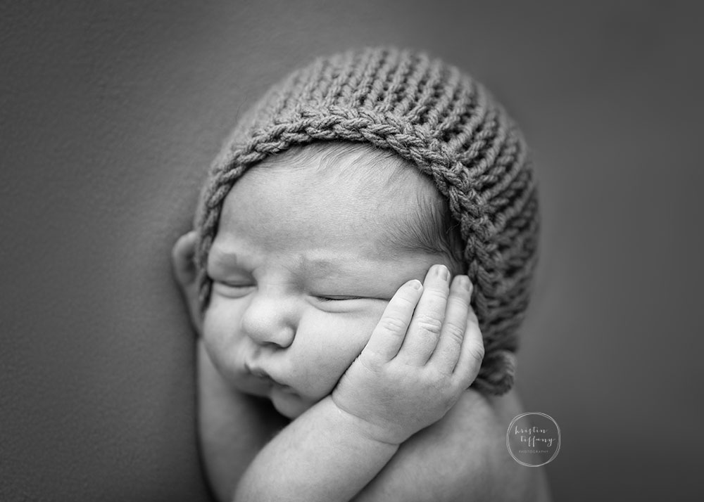 a photo of a newborn boy in a bonnet with his hands on his cheeks