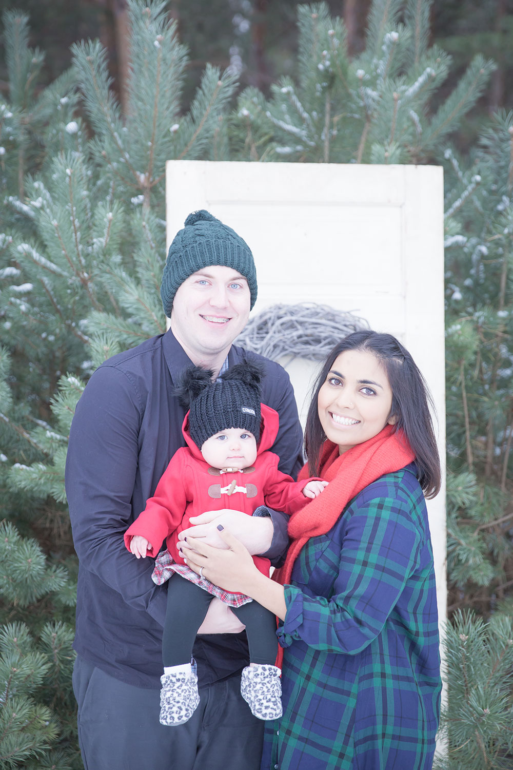 a photo of a young family outside in winter by an old wooden door in the woods