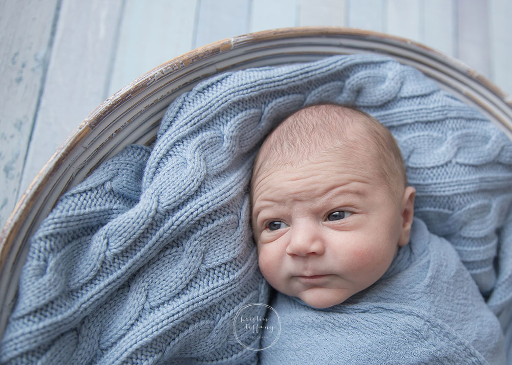 a photo of a wide eyed newborn baby boy in a prop bowl