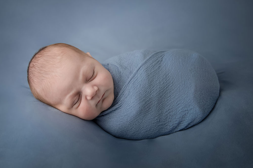 a photo of a swaddled newborn baby boy posed on blue