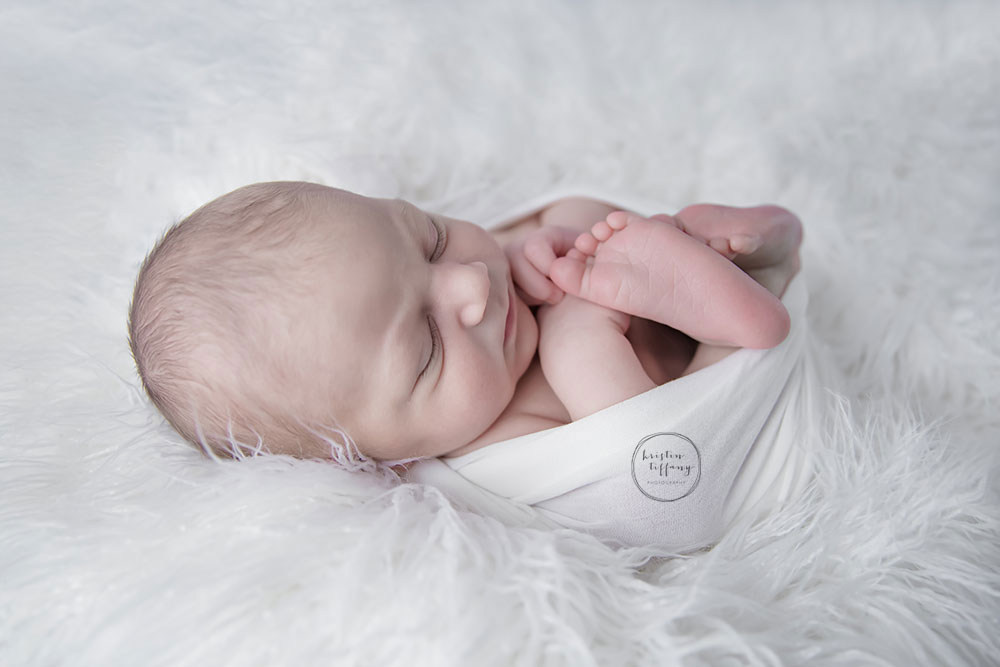a photo fo a swaddled newborn posed on white fur