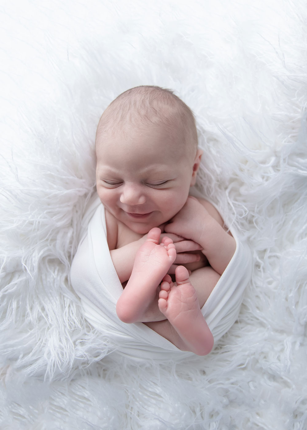 a photo of a newborn baby boy curled up and smiling