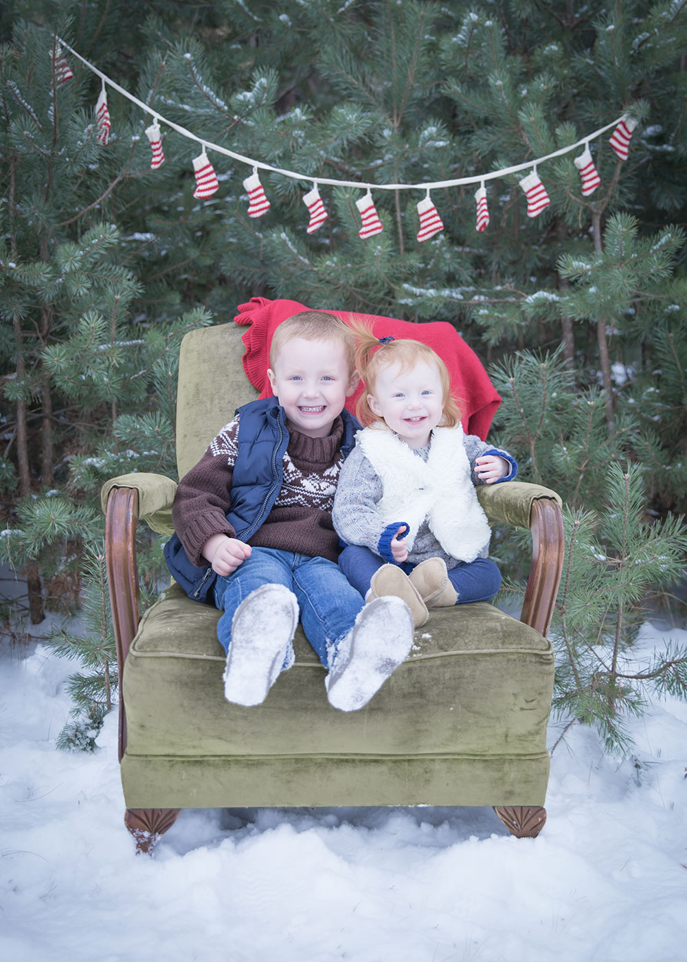 a photo of young siblings sitting in an armchair outside in the snow
