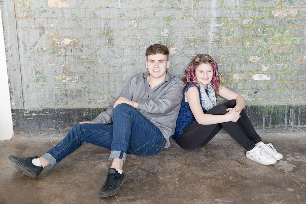 a photo of teenaged siblings by a brick wall