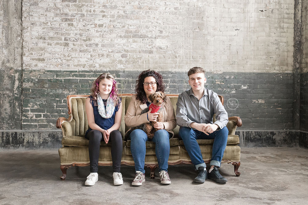 a photo of a family sitting on a vintage couch by a distressed brick wall
