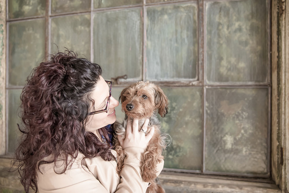a photo of a woman holding her dog by an old distressed window
