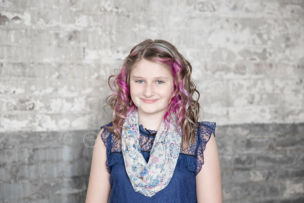 a photo of a young lady standing by a brick wall