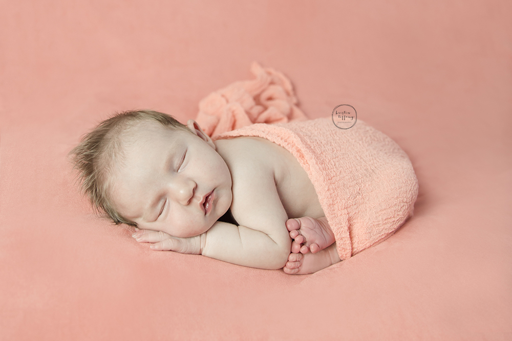 a photo of a newborn baby girl posed on a peach backdrop