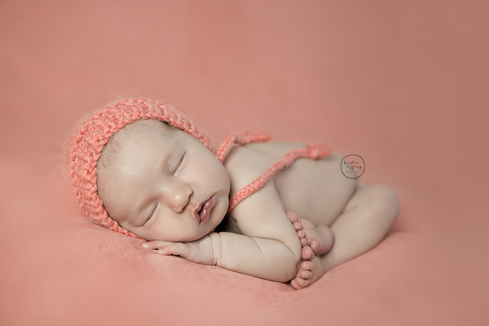a photo of a newborn baby girl posed in a coral bonnet