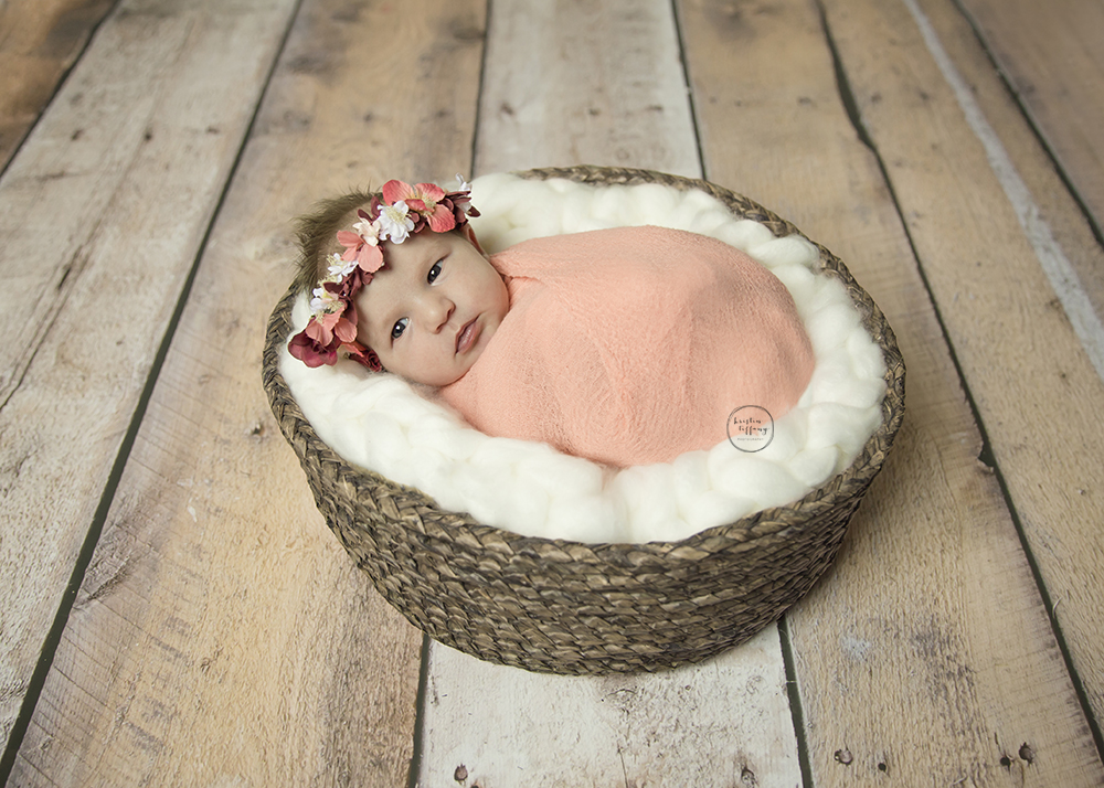 a photo of a newborn baby girl posed in a basket with a floral crown