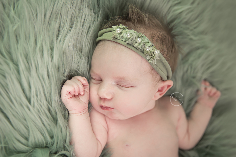 a photo of a newborn baby girl sleeping on a green fur blanket