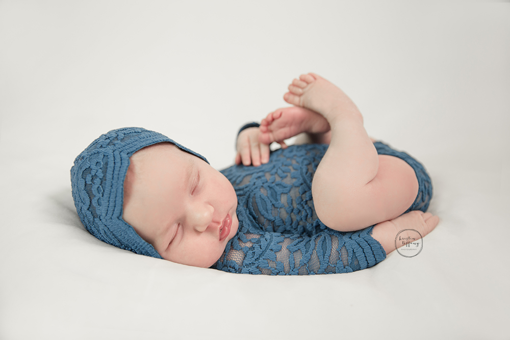 a photo of a newborn baby girl posed in a lace romper and bonnet