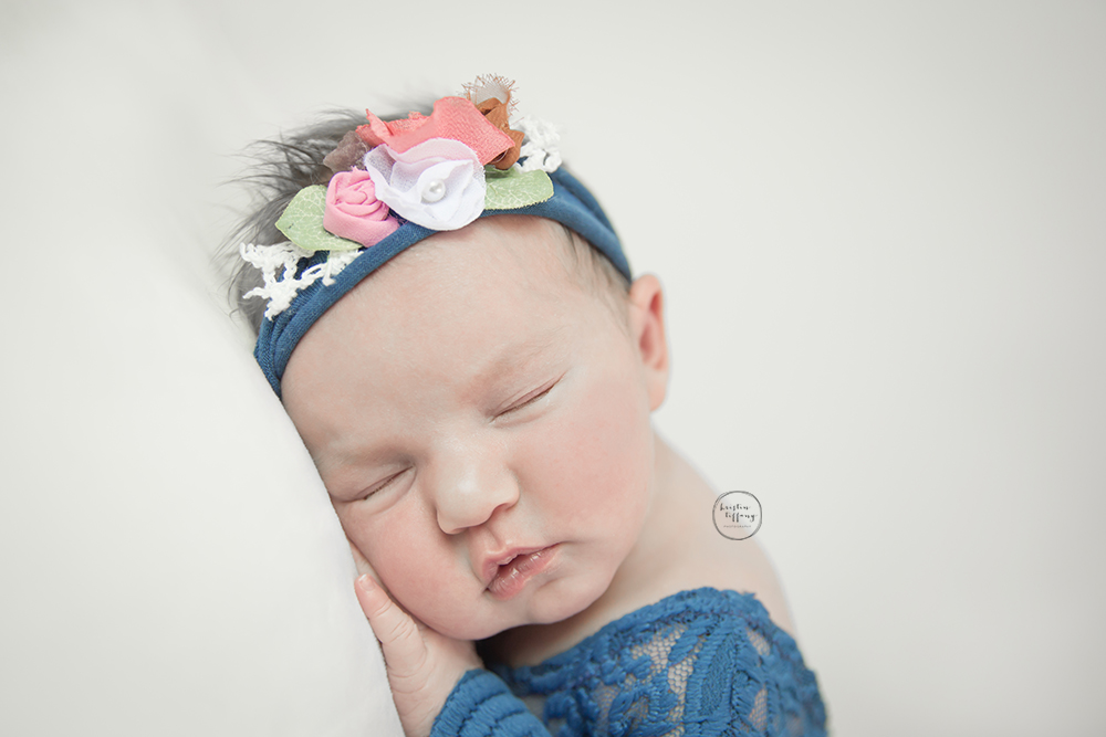 a photo of a newborn baby girl posed sleeping with a floral tieback