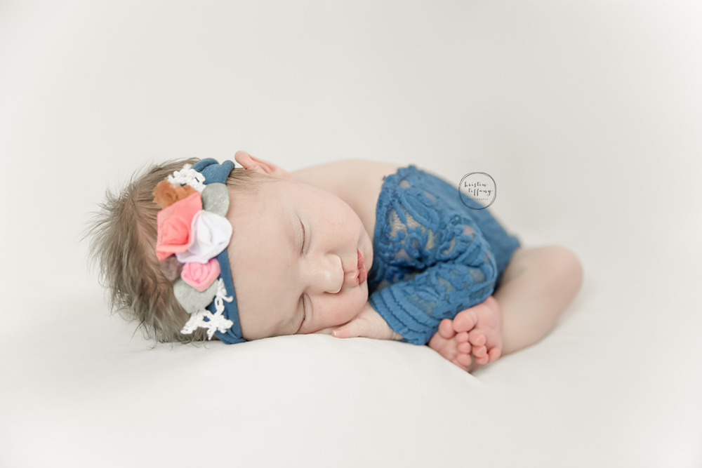 a photo of a newborn baby girl posed in a lace romper